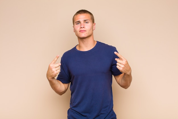 Photo blonde  man with a bad attitude looking proud and aggressive, pointing upwards or making fun sign with hands