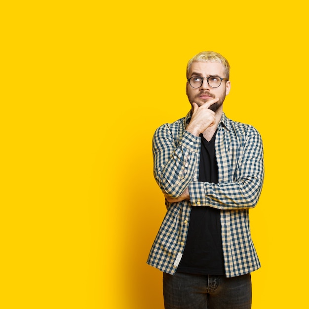 Blonde man with beard and eyeglasses is looking thoughtful touching his chin