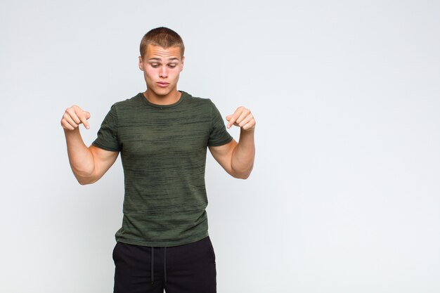 Blonde man with open mouth pointing downwards with both hands, looking shocked, amazed and surprised