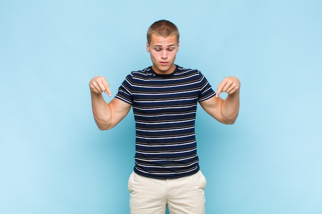 Blonde man with open mouth pointing downwards with both hands