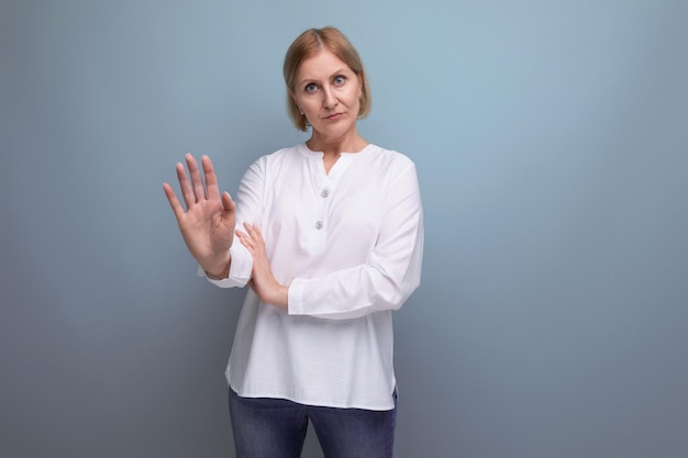 Blonde middle aged woman in white blouse with denial gesture on studio background