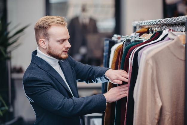 L'uomo millenario biondo in un abbigliamento da lavoro sceglie i vestiti in un negozio l'uomo sta facendo shopping