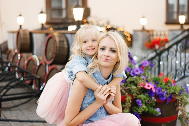 Blonde moeder en dochtertje in roze rokken en denimoverhemden.