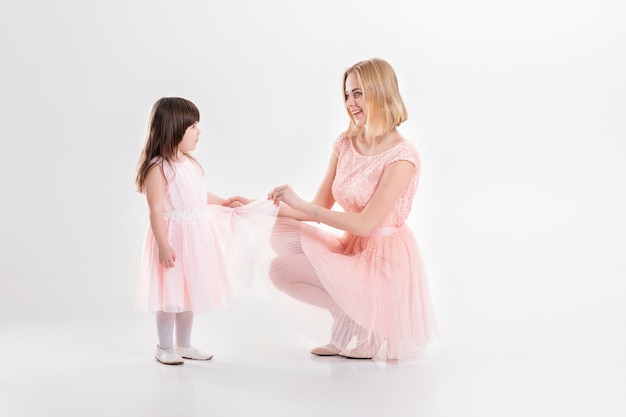 Blonde moeder en lief dochtertje in roze jurken prinsessen knuffelen en lachen op een grijze achtergrond. familie