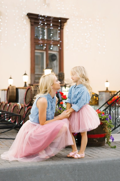 ブロンドのママとピンクのスカートとデニムのシャツを着た小さな娘がお互いを見つめる