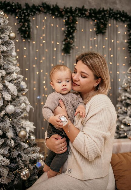 Blonde mom sits on the couch and hugs a baby boy on a New Year's background