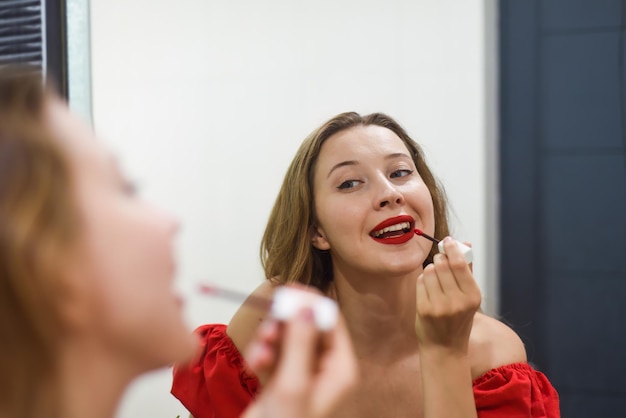 Blonde mooie vrouw die een rode lippenstift aanbrengt en naar de spiegel kijkt