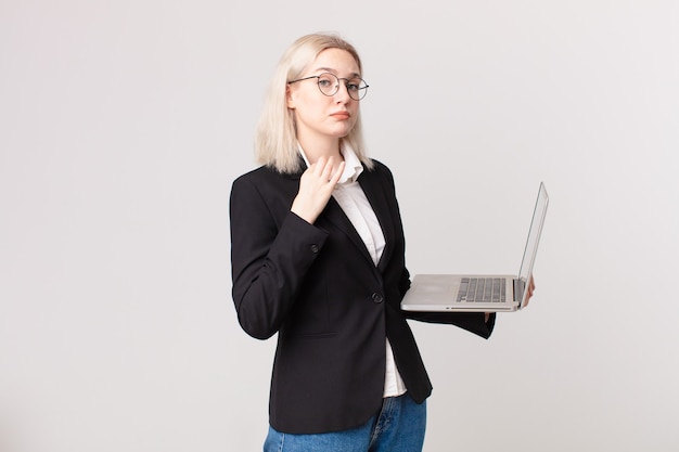 Blonde mooie vrouw die er arrogant, succesvol, positief en trots uitziet en een laptop vasthoudt