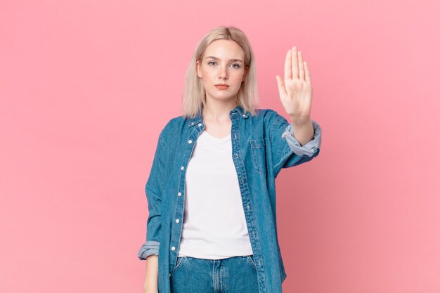 Blonde mooie vrouw die er serieus uitziet en open palm toont die een stopgebaar maakt