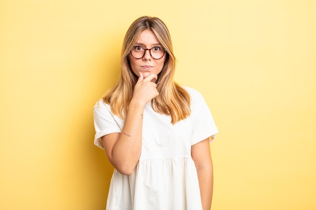 Blonde mooie vrouw die er serieus, verward, onzeker en attent uitziet, twijfelend tussen opties of keuzes