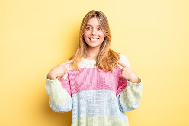 Blonde mooie vrouw die er trots, positief en casual uitziet en met beide handen naar de borst wijst