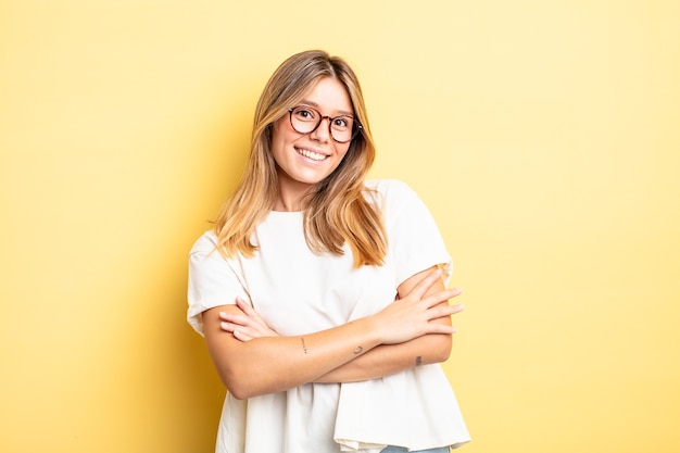 Blonde mooie vrouw die gelukkig lacht met gekruiste armen, met een ontspannen, positieve en tevreden pose