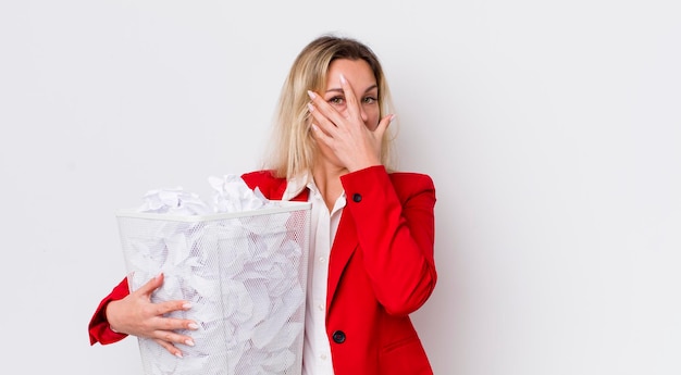 Blonde mooie vrouw die geschokt, bang of doodsbang kijkt en haar gezicht bedekt met handpapieren ballen, foutenconcept