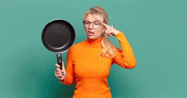 Blonde mooie vrouw die kok met een pan leert