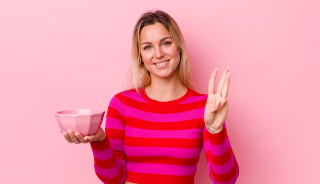 Blonde mooie vrouw die lacht en er vriendelijk uitziet met nummer drie leeg komconcept