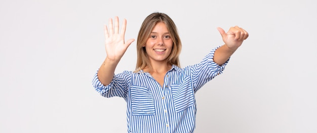 Blonde mooie vrouw die lacht en er vriendelijk uitziet, nummer zeven of zevende toont met de hand naar voren, aftellend