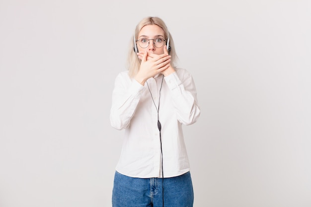 Blonde mooie vrouw die mond bedekt met handen met een geschokt telemarketingconcept