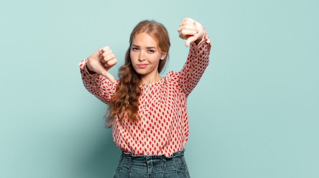 Blonde mooie vrouw die verdrietig, teleurgesteld of boos kijkt, duimen naar beneden toont in onenigheid, zich gefrustreerd voelt