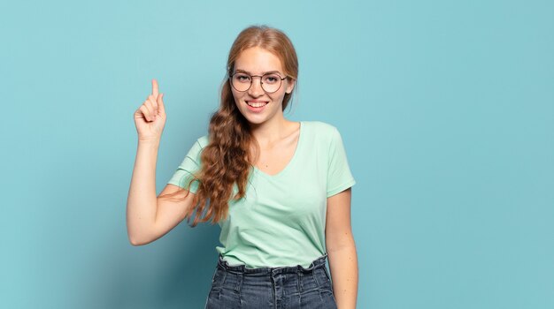 Blonde mooie vrouw die vrolijk en gelukkig glimlacht, naar boven wijzend met één hand om ruimte te kopiëren