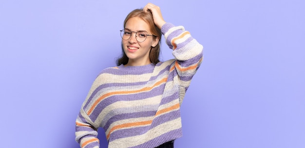 Blonde mooie vrouw die vrolijk en nonchalant glimlacht, hand aan hoofd met een positieve, vrolijke en zelfverzekerde blik