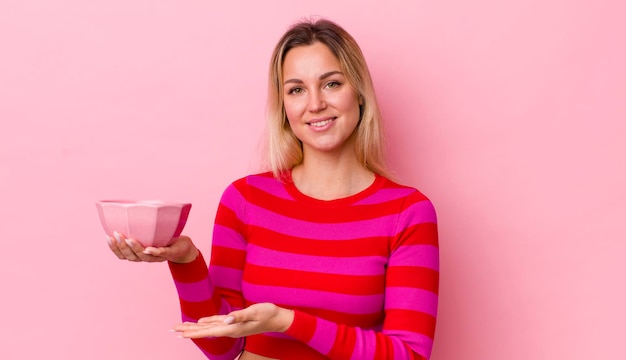 Blonde mooie vrouw die vrolijk lacht en zich gelukkig voelt en een concept lege kom toont