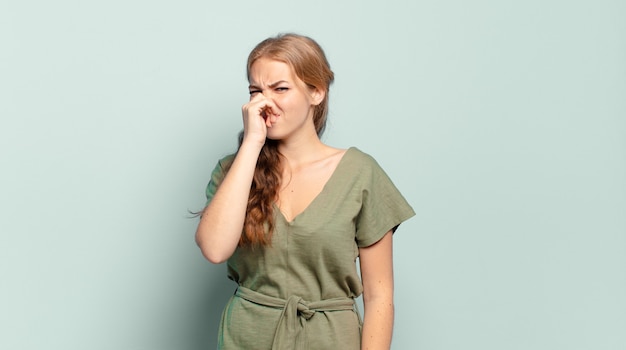 Blonde, mooie vrouw die walgt en neus vasthoudt om te voorkomen dat ze een vieze en onaangename stank ruikt