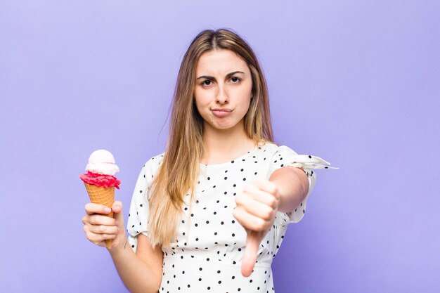 Blonde, mooie vrouw die zich boos, boos, geïrriteerd, teleurgesteld of ontevreden voelt, duimen naar beneden toont met een serieuze blik