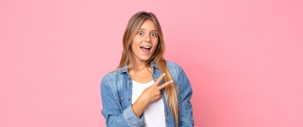 Blonde mooie vrouw die zich gelukkig, positief en succesvol voelt, met de hand die een v-vorm over de borst maakt, overwinning of vrede toont