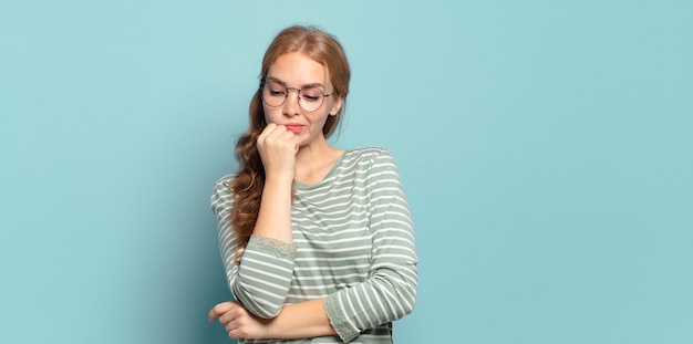 Blonde mooie vrouw die zich serieus, attent en bezorgd voelt, zijwaarts starend met de hand tegen de kin gedrukt