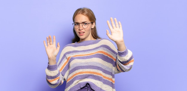 Blonde, mooie vrouw die zich stomverbaasd en bang voelt, bang is voor iets beangstigend, met de handen open en zegt: blijf weg