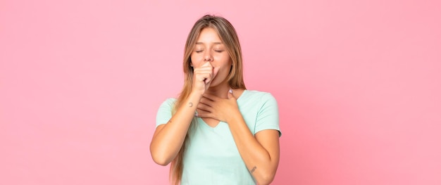 blonde mooie vrouw die zich ziek voelt met een zere keel en griepsymptomen, hoest met bedekte mond