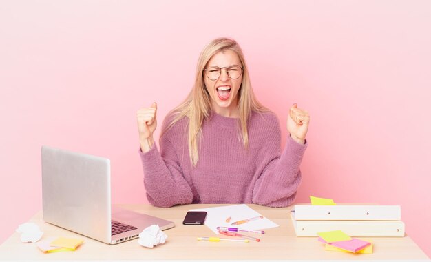 blonde mooie vrouw jonge blonde vrouw die agressief schreeuwt met een boze uitdrukking en met een laptop werkt