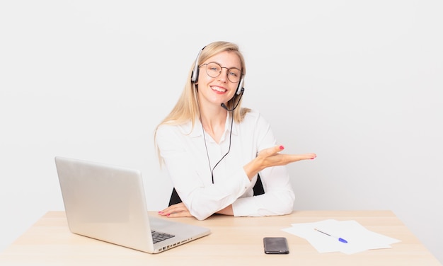 Blonde mooie vrouw jonge blonde vrouw die vrolijk lacht, zich gelukkig voelt en een concept toont en met een laptop werkt