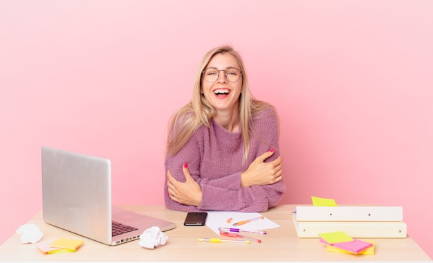 Blonde mooie vrouw jonge blonde vrouw hardop lachen om een hilarische grap en werken met een laptop