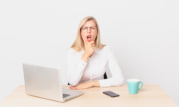 Blonde mooie vrouw jonge blonde vrouw met mond en ogen wijd open en hand op kin en werken met een laptop