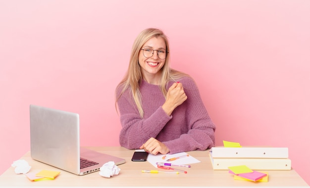 Blonde mooie vrouw jonge blonde vrouw voelt zich gelukkig en staat voor een uitdaging of viert en werkt met een laptop