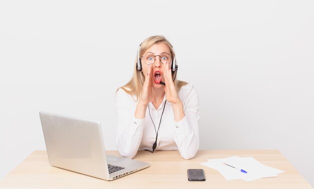 Blonde mooie vrouw jonge blonde vrouw voelt zich gelukkig, geeft een grote schreeuw met de handen naast de mond en werkt met een laptop