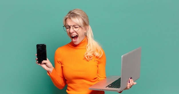 Blonde mooie vrouw met een cel en laptop