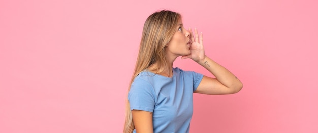 Foto blonde mooie vrouw profielweergave, blij en opgewonden kijkend, schreeuwend en bellend om ruimte aan de zijkant te kopiëren