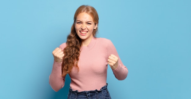 blonde mooie vrouw triomfantelijk schreeuwen, lachen en zich blij en opgewonden voelen terwijl ze succes viert