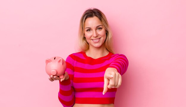 Blonde mooie vrouw wijzend op de camera die je spaarvarken concept kiest