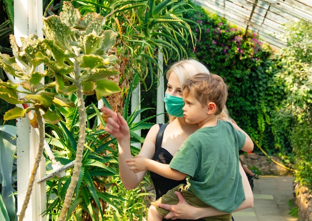 Blonde mother in face mask with a child in palm greenhouse of the Botanical garden