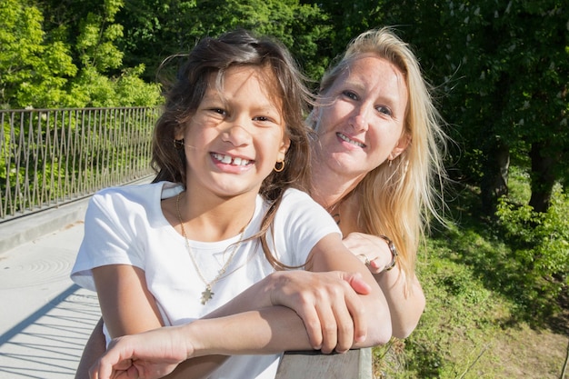 Blonde mother with her black-haired girl tan in the park