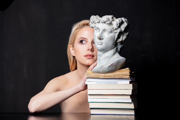 Blonde naast een antieke buste van een man op boeken