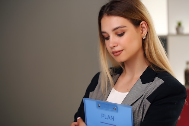 Blonde in the office and jacket holding documents.