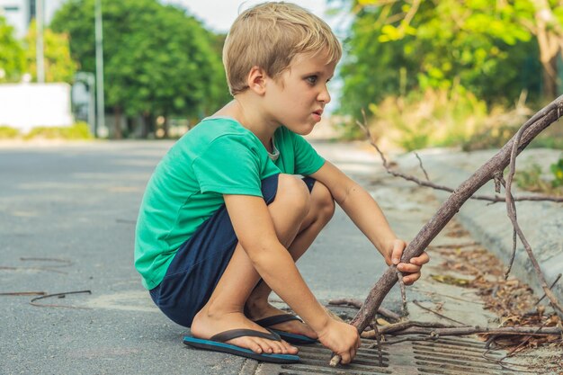 Blonde ondeugende jongen grappenmaker met sproeten spelen duwt stok naar beneden weg afvoer artistieke emoties gezichtsuitdrukking gebaren Familie relatie micro momenten van de kindertijd menselijkheid samenleving