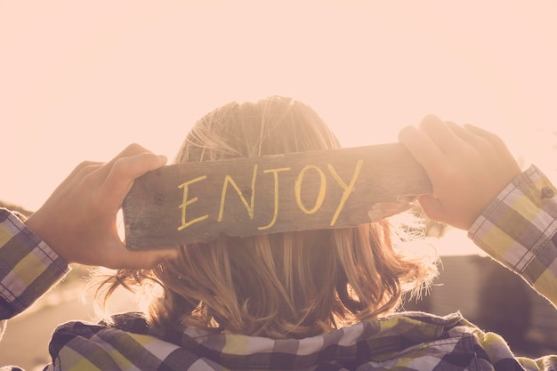blonde people young teenager with enjoy written on a natural piace of recycled wood feeling and golden sunset atmosphere image for positive life and vibes concept and message
