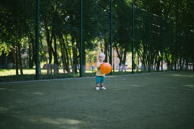 blonde peuter rent vrolijk over het sportveld met een grote bal in zijn handen