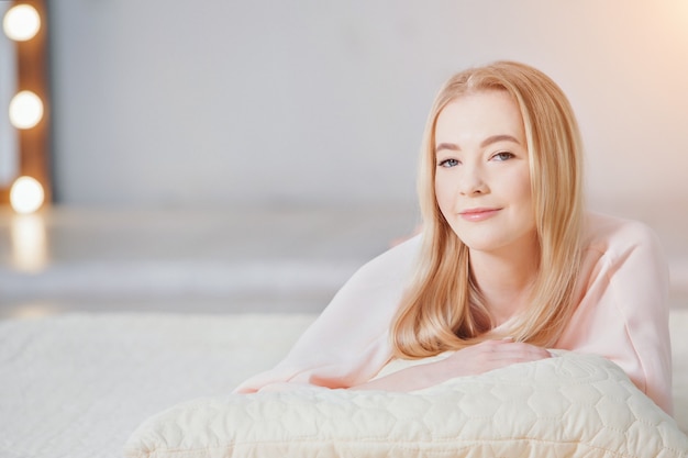 The blonde in pink is lying on the floor. the girl smiles. beauty and health of the face, hair, and skin. copy space