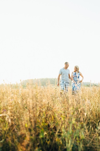Беременная блондинка-мама в голубом платье и мужчина в поле
